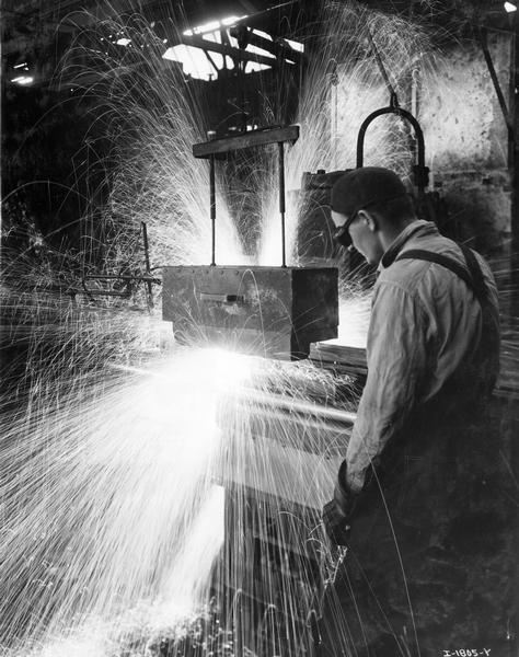 Sparks fly from a machine operated by a worker inside International Harvester's Tractor Works.