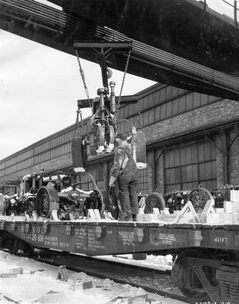 Worker guiding a new Farmall 20 tractor suspended from a crane onto a snow-covered railroad car outside International Harvester's Tractor Works.