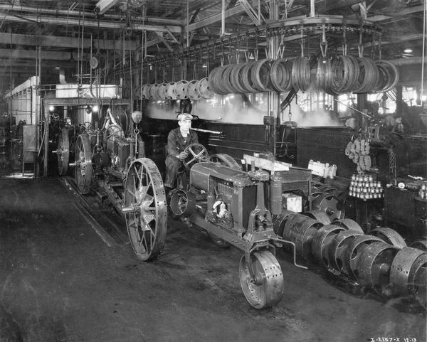 Worker driving a Farmall F-12 tractor off of the assembly line at International Harvester's Tractor Works.