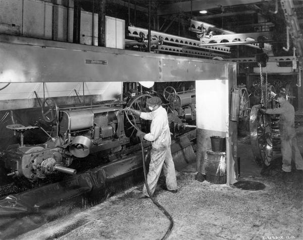 Worker spray painting a Farmall F-12 tractor while others attach rear wheels along an assembly line at International Harvester's Tractor Works.