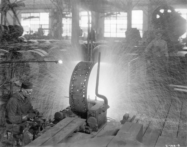 Worker welding a steel tractor wheel in a shower of sparks at International Harvester's Tractor Works.