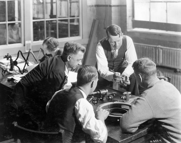 Four engineers(?) gathered around an office table to examine a part at International Harvester's Tractor Works.