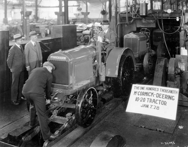 100,000th McCormick-Deering 10-20 HP tractor coming off of the assembly line at International Harvester's Tractor Works. The tractor came off at 10:32 a.m. Mr. E.C. Lutz, Superintendent of the works, is behind the wheel of the tractor. Mr. A.C. Richmond, Chief Inspector, is the first man from the left, and Mr. C.H. Smart, Assistant Works' Manager, is second from the left; both facing the tractor. Mr. W.F. Hoshel, General Foreman, is cranking the tractor.