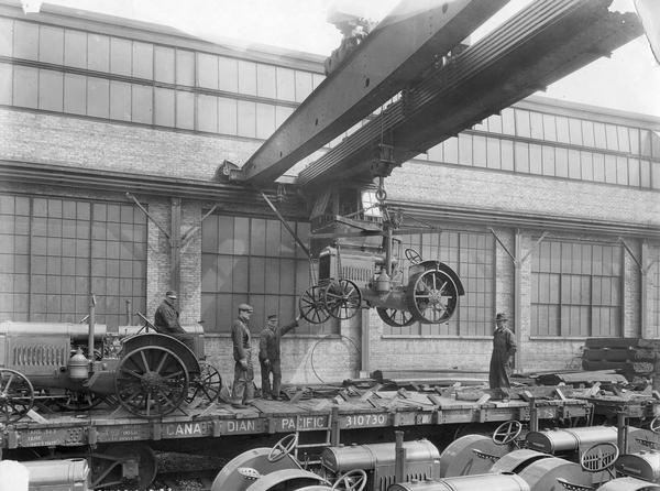 Workers lowering McCormick-Deering 10-20 HP tractors onto railroad cars for shipment using an overhead crane at International Harvester's Tractor Works.