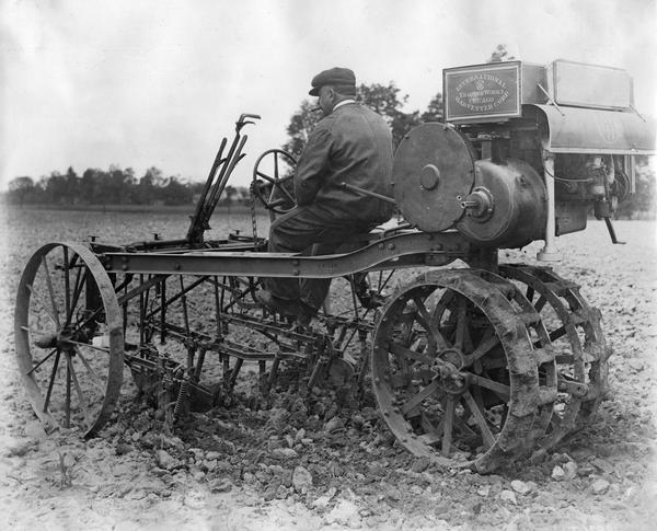 Man with cigar tests an International Harvester experimental motor cultivator in a field.
