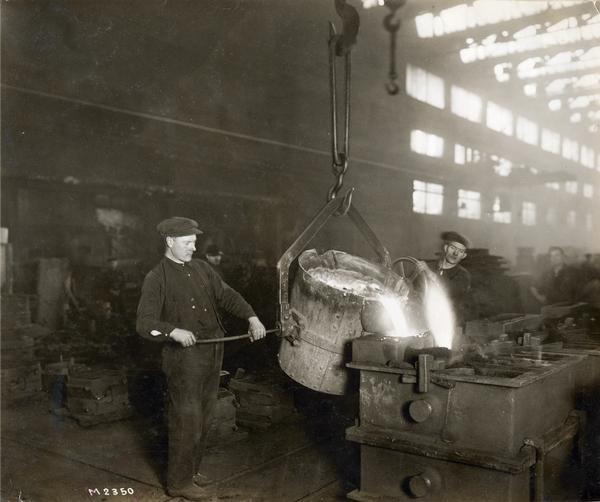 Two workers pouring molten metal from a crane-held vat into a mold to make castings at International Harvester's Milwaukee Works. The factory was owned by the Milwaukee Harvester Company before 1902.