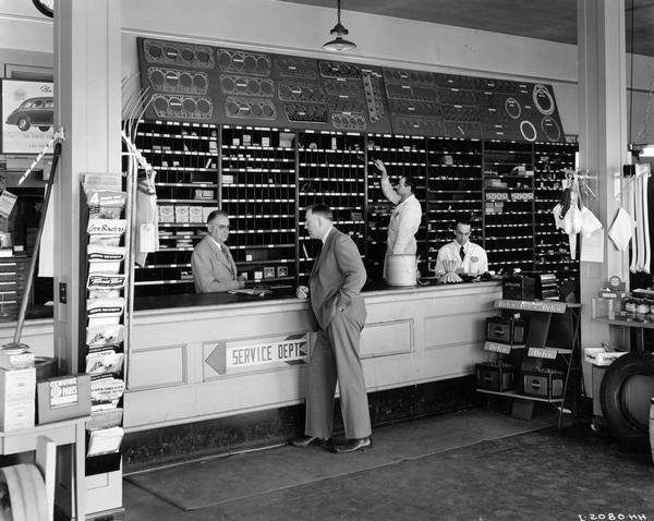 Employees at the parts counter of the  International Harvester McCormick-Deering dealership of Hammer-Staunton Farm & Ranch Equipment. Ed Hammer, the proprietor of dealership, is behind the counter talking with W.F. Koch, IHC branch manager at Billings.