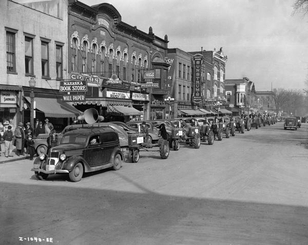 Men driving Farmall tractors (including the Farmall A) in a parade through downtown Oskaloosa as townspeople look on. The parade is led by a truck with a loudspeaker mounted on the roof.