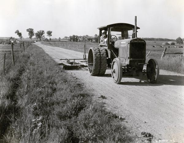 Worker grading a rural road with a McCormick-Deering Model 30 industrial tractor and a pull grader. The tractor was owned by Weld County.