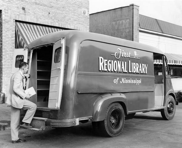 Man with a book in his hand entering the rear of International Metro LM series delivery truck owned and operated by the First Regional Library of Mississippi.