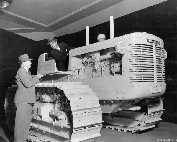 Eddie Cantor mugging on an International TD-18 diesel crawler tractor at the National Roadbuilders Show. Mr. Gainsford of the Los Angeles branch house is pointing out the features of the tractor to Mr. Cantor.