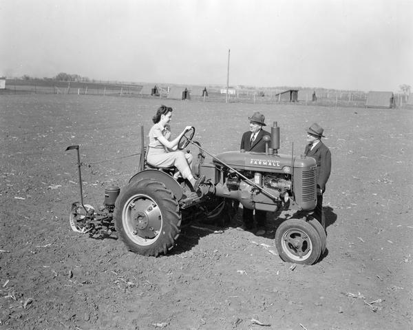 Woman sitting on a Farmall B tractor with attached corn planter talking with International Harvester dealers Henry Brosnahan, Manager (left), and Jack Callahan, Assistant Manager (right).