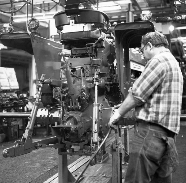 Assembly line worker greasing a three point arm link on a Farmall 66 series tractor - possibly a 1066.