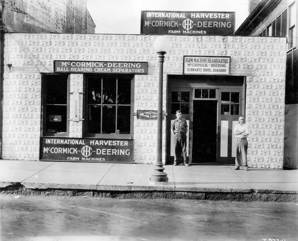 Two employees standing on the sidewalk in front of the storefront of an International Harvester dealership owned by the Schwartz Bros. The dealership sold McCormick-Deering farm machines.