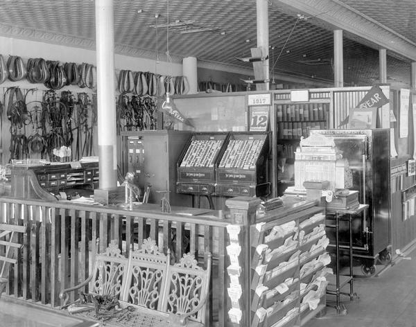 Interior of the Maxwell Implement Company, an International Harvester dealership, with desks, literature racks, a cash register, and merchandise. The dealership was under the jurisdiction of the company's South Bend branch house.