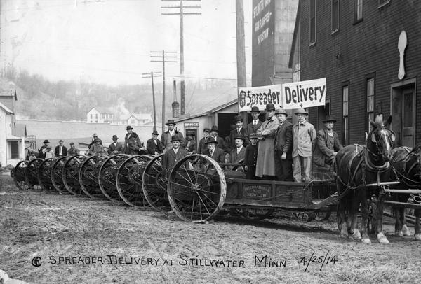 Farmers posing with their new International horse-drawn manure spreaders in the streets of a rural town. The "spreader delivery" day was organized for publicity by the local International Harvester dealer. An International No. 3 New Low manure spreader is in the foreground.