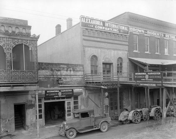 Elevated view of trucks and Fordson tractors parked in the street in front of the International Harvester dealership of the Alexandria International Company, Inc. Signs on the building advertise McCormick-Deering farm machines and Chattanooga Chilled Plows.