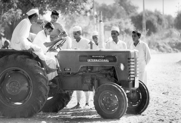 The original caption reads: "Under a Banyan tree by the village well, neighboring farmers look over a farm tractor, first India-made one they have seen. This unit is produced by International Tractor Company of India, Ltd., a joint venture company which has a plant near Bombay.