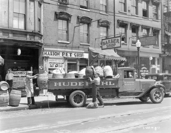 Men unloading barrels of Hudepohl beer from an International B-4 truck in front of the "Bay Horse Exchange." Other stores on the city street include the Marion Pet Shop, a barber shop, Philip Weber cutlery and grinding, and the United Chili Parlor and Lunch Room. This B-4 truck was equipped with a 170-inch wheel base. It was owned by the Hudepohl Brewing Company.
