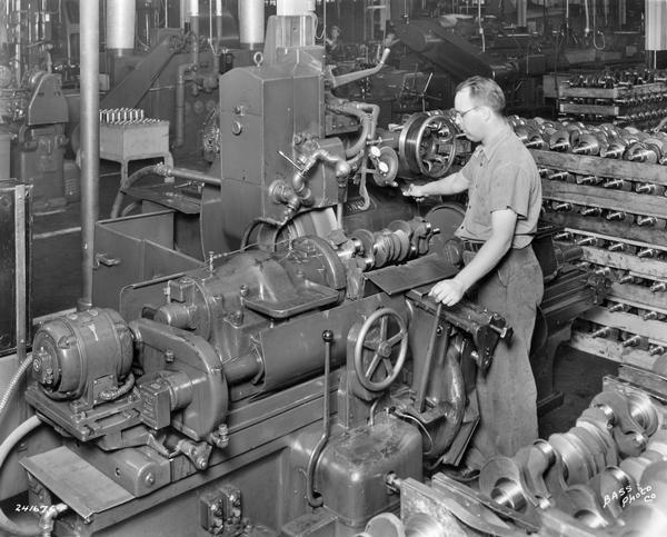Worker operating a hydraulic Landis machine for grinding pin bearings on crankshafts at International Harvester's Indianapolis Works. The Indianapolis Works was built in 1937 to produce truck engines.