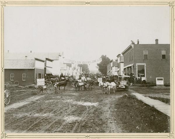 Crowd gathered on the main street to witness the delivery of McCormick binders, mowers and other machines to customers. McCormick Harvesting Machine Company agents organized these events — which often included parades, music and food — to publicize the company and its products. This "McCormick Day" was organized by agents Gullickson and Thompson. A boy is holding a sign proclaiming: "McCormick binders, mowers and rakes, the Dewey of them all."