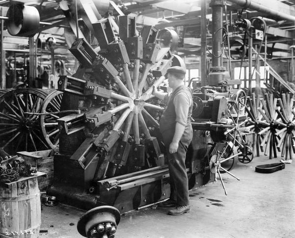 Worker inserting spokes into a wagon wheel apparatus at International Harvester's Accurate Engineering Works.