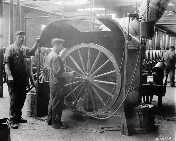 Workers spray-painting a wagon wheel inside the paint room at International Harvester's Accurate Engineering Works.