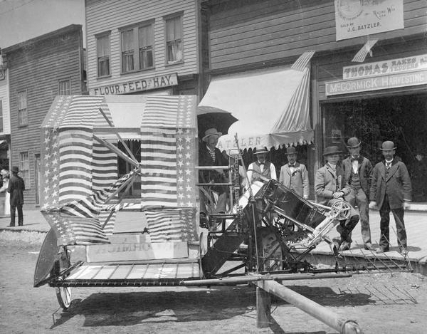 McCormick grain binder decorated with stars and stripes on the street in front of a McCormick Harvesting Machine Company dealership. The location is possibly Racine.