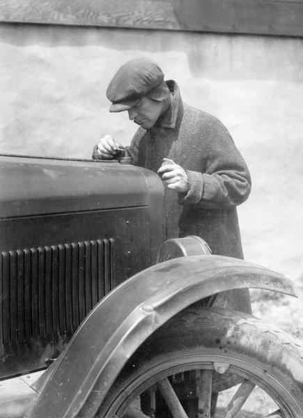 Staged scene of a man looking into an automobile radiator with a match in hand. This photograph was taken for International Harvester's Agricultural Extension Department. It was used to warn families of potential farm hazards. The original caption reads: "Don't look in auto radiator with match in winter. Alcohol radiator might catch fire."