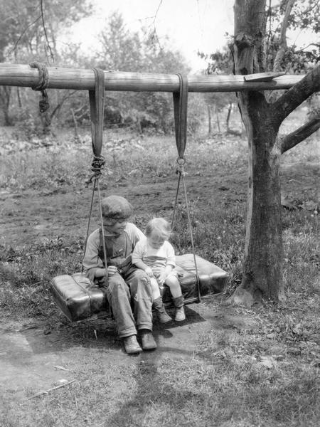 Young boy and a toddler relaxing on a homemade tree swing made with an automobile seat.