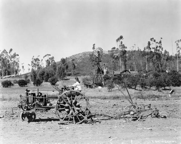 Eighteen-year-old Juanita Washington operating a McCormick-Deering Farmall F-12 with attached plow. According to the original caption, Ms. Washington "regularly operates the tractor for producing crops on a 25-acre truck farm. Her mother markets the produce and her brother works in a grocery in El Cajon where some of the crops grown are sold."
