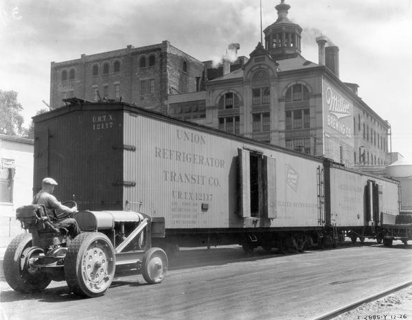 Worker on an International I-30 industrial tractor used for "spotting" freight cars around the Miller Brewing Company. Two refrigerated rail cars are parked outside the factory building.