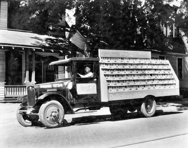 Driver delivering cases of bottled Coca-Cola (soda) to a residential neighborhood in an International delivery truck.