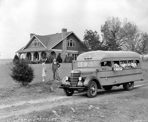 International D-30 school bus with Hicks body picking up a boy and girl outside a rural house.