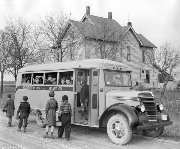 Children getting off an International D-30 school bus in front of a rural farmhouse. The bus served Washington township in Grant County, Indiana. The bus featured a 155-inch wheelbase and a Wayne 17-foot body with a 40-passenger capacity.