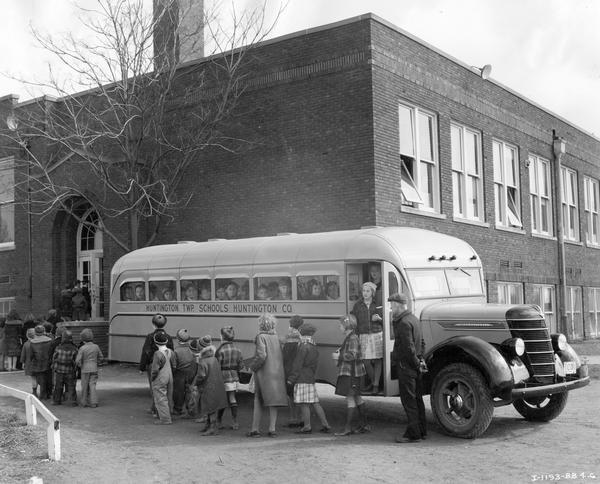 Students getting off an International D-30 school bus outside their school building. The bus served Huntington township in Huntington County, Indiana. The bus featured a 191-inch wheelbase and a 22-foot body with a 48-passenger capacity.