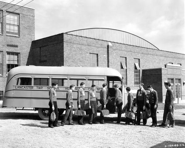 Members of the Lancaster High School basketball team in letter sweaters boarding an International D-30 school bus outside a gymnasium. The bus served Lancaster township in Huntington County, Indiana. The bus featured a 173-inch wheelbase and a 19-foot Hicks body with a 42-passenger capacity.