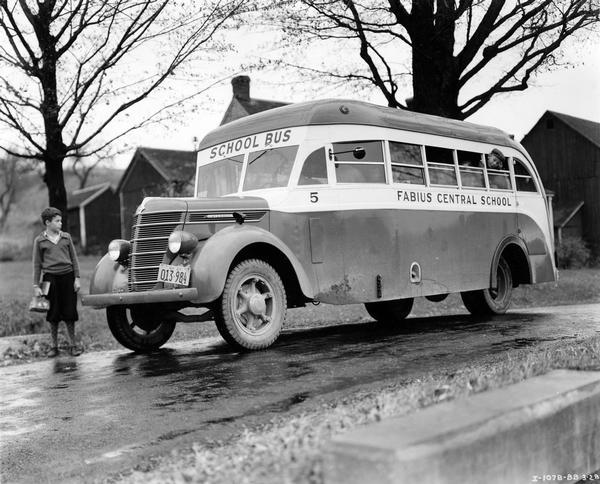 Boy with a book and lunch pail waiting as an International D-30-B or D-35-B school bus pulls up in front of his rural farmhouse. Another mischievous lad is sticking his head out of the bus window. The bus served the Fabius Central School. It featured a 173-inch wheelbase and a 31-passenger capacity.