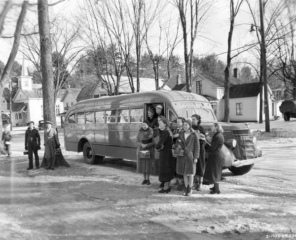 Hadley-Luzerne Central School students with books and lunch pails getting off of an International D-40 school bus. The bus featured a 215-inch wheelbase and a 49-passenger capacity.