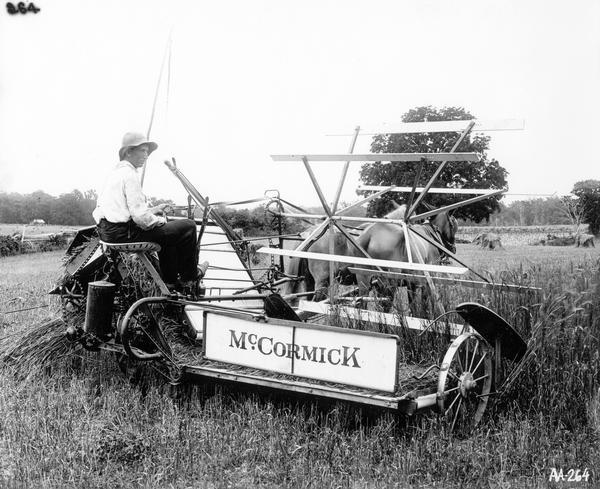 Young farmer in a field harvesting grain with a horse-drawn McCormick grain binder.