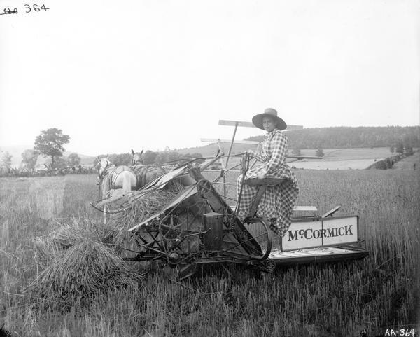 Woman in a hat and dress sitting on a horse-drawn McCormick grain binder.