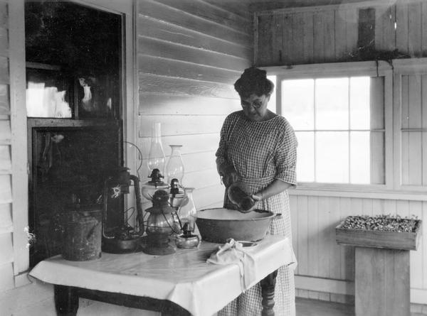 Woman cleaning kerosene lamps on the front porch(?) of her house.