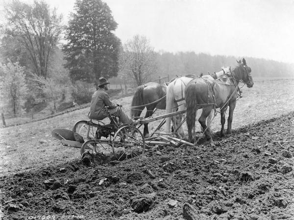 Farmer working in a field with an Oliver plow drawn by three horses.