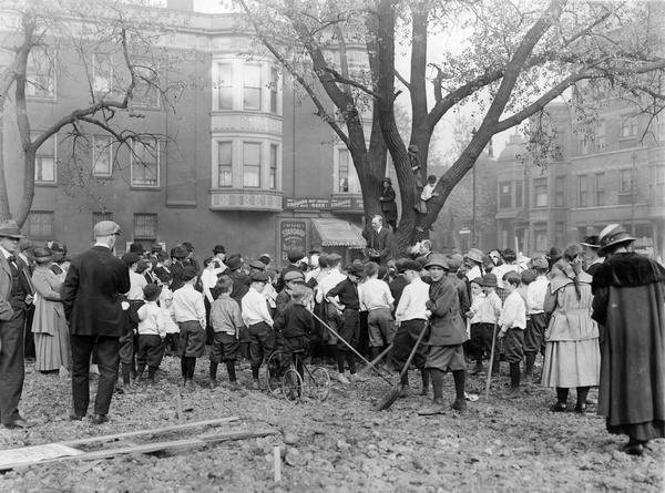 Large crowd of school children and adults gathered for a school garden dedication. Original caption reads: "Mr. Prost making a talk at a garden dedication at the corner of Adams and Kedzie Sts. This garden was conducted by the Marshall School." One boy seems to be blowing a "raspberry" at the camera while another is sitting on his tricycle.