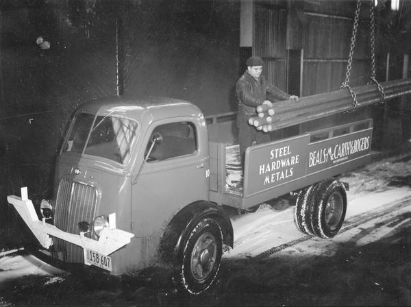 Worker unloading steel beams from the back of an International D-300 truck at night. The truck was owned by Beals-McCarthy & Rogers Co., a wholesale hardware company.