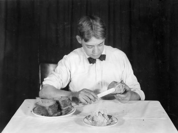 A young man sitting at a table buttering a slice of bread.