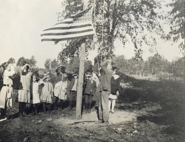 Miss Summers' pupils saluting as an American flag is raised outside Pleasant View School. The original caption reads: "Loyal U.S. citizens in the making."