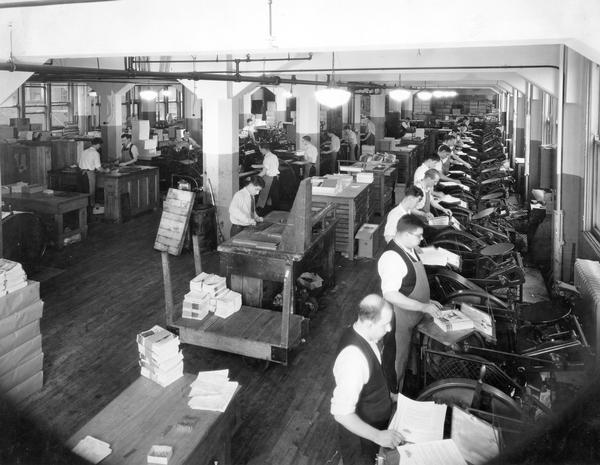 Male workers in a printing room at International Harvester's "Harvester Press." Some of the men appear to be printing advertising brochures for McCormick-Deering cream separators.