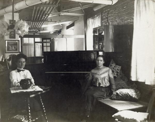 Two women sitting in the "rest room" at the McCormick Reaper Works. A piano is in the background.