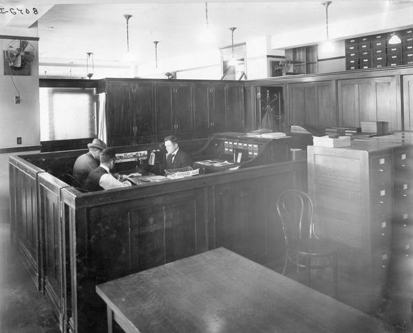 Three men meeting at a desk in a cubicle in an International Harvester Company office.